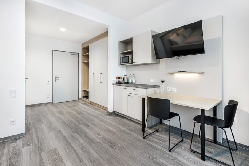 Helles Hotelzimmer mit Tisch, Stühlen und Küchenzeile.