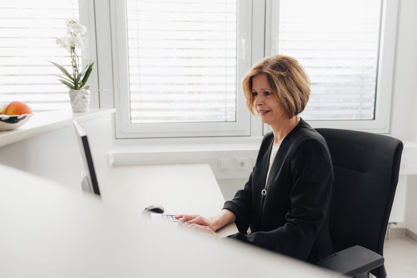 Frau mit blonden Haaren sitzt am Schreibtisch und arbeitet am Computer.