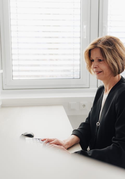 Frau mit blonden Haaren sitzt am Schreibtisch und arbeitet am Computer.