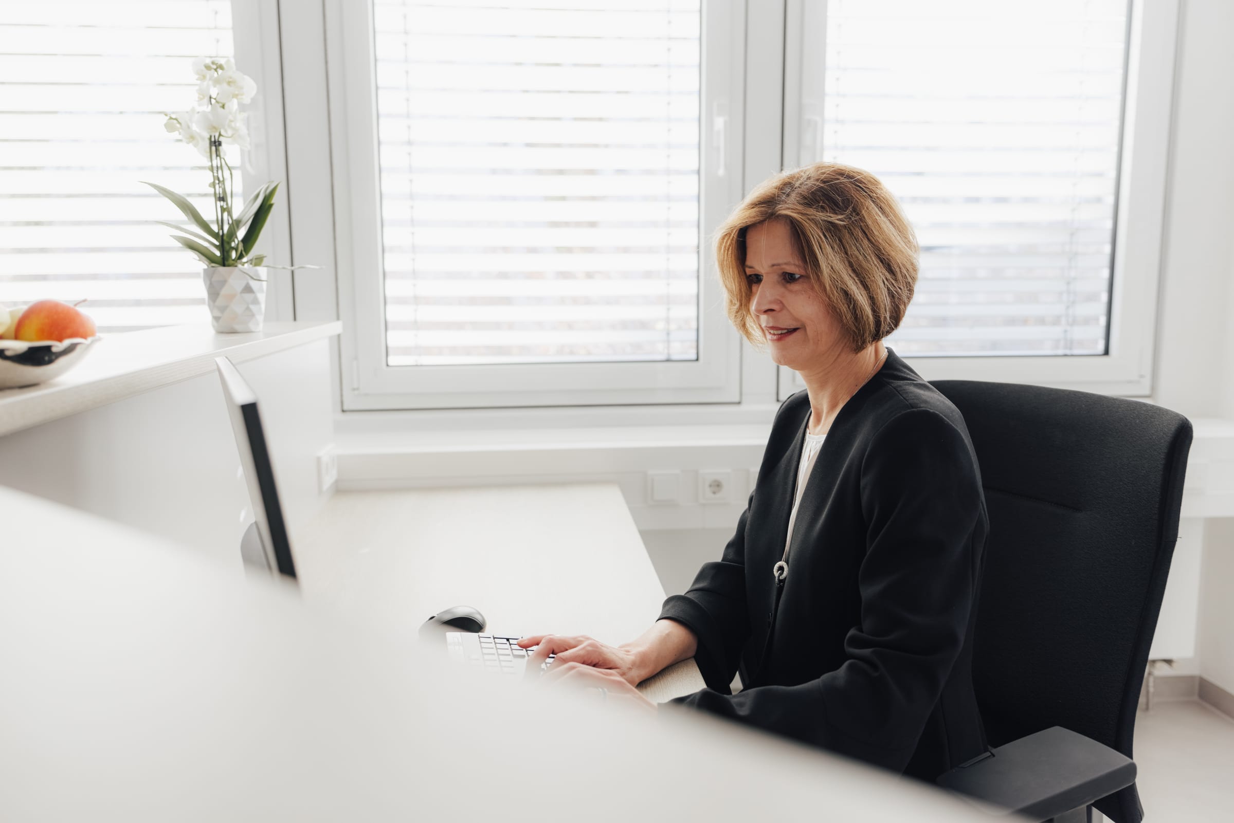 Frau mit blonden Haaren sitzt am Schreibtisch und arbeitet am Computer.