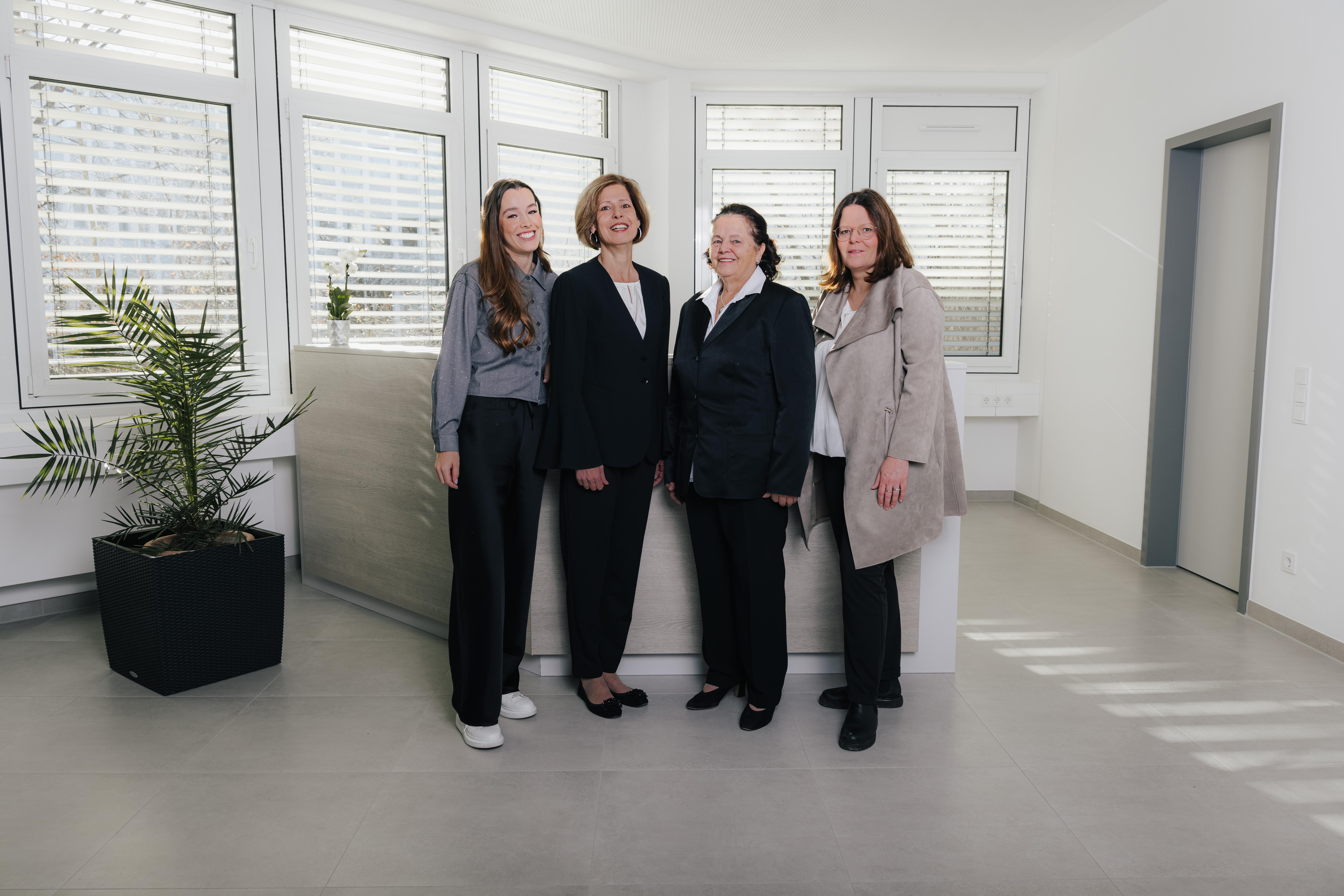 Vier Frauen stehen in einem modernen Büro vor einem Empfangstresen.