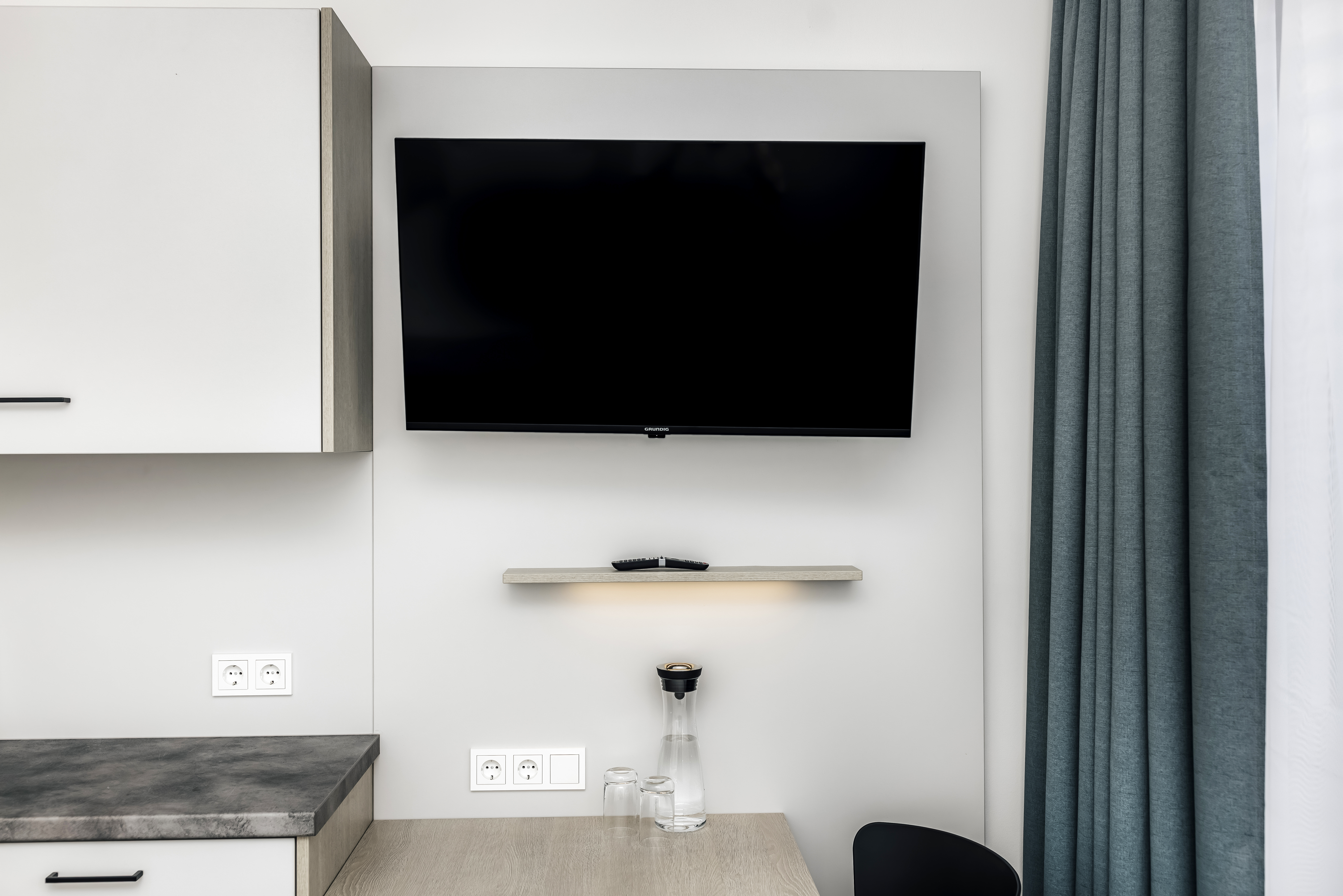 Hotelzimmer mit Fernseher, Tisch und Vorhängen.