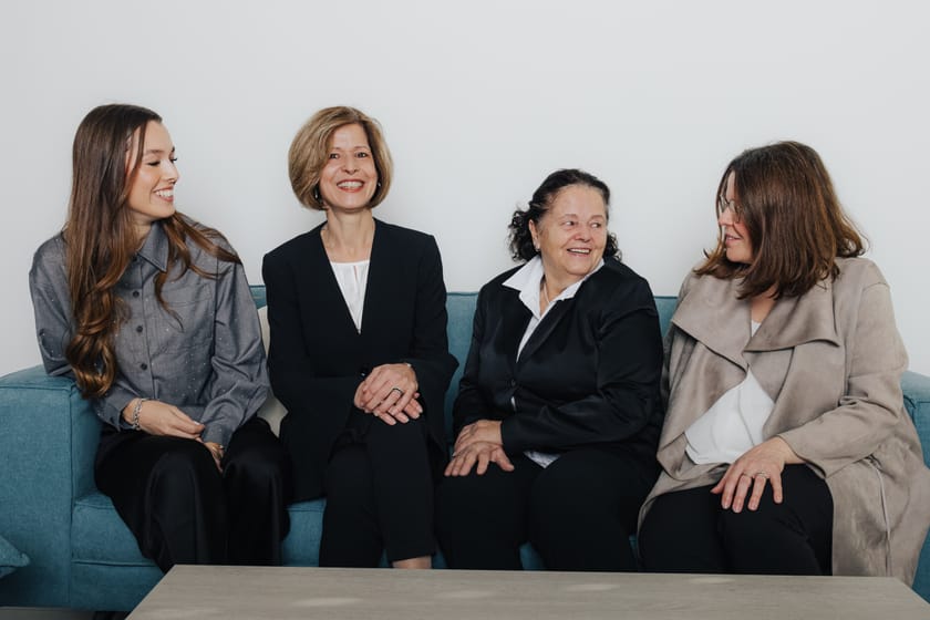 Vier Frauen in formeller Kleidung sitzen auf einem blauen Sofa.