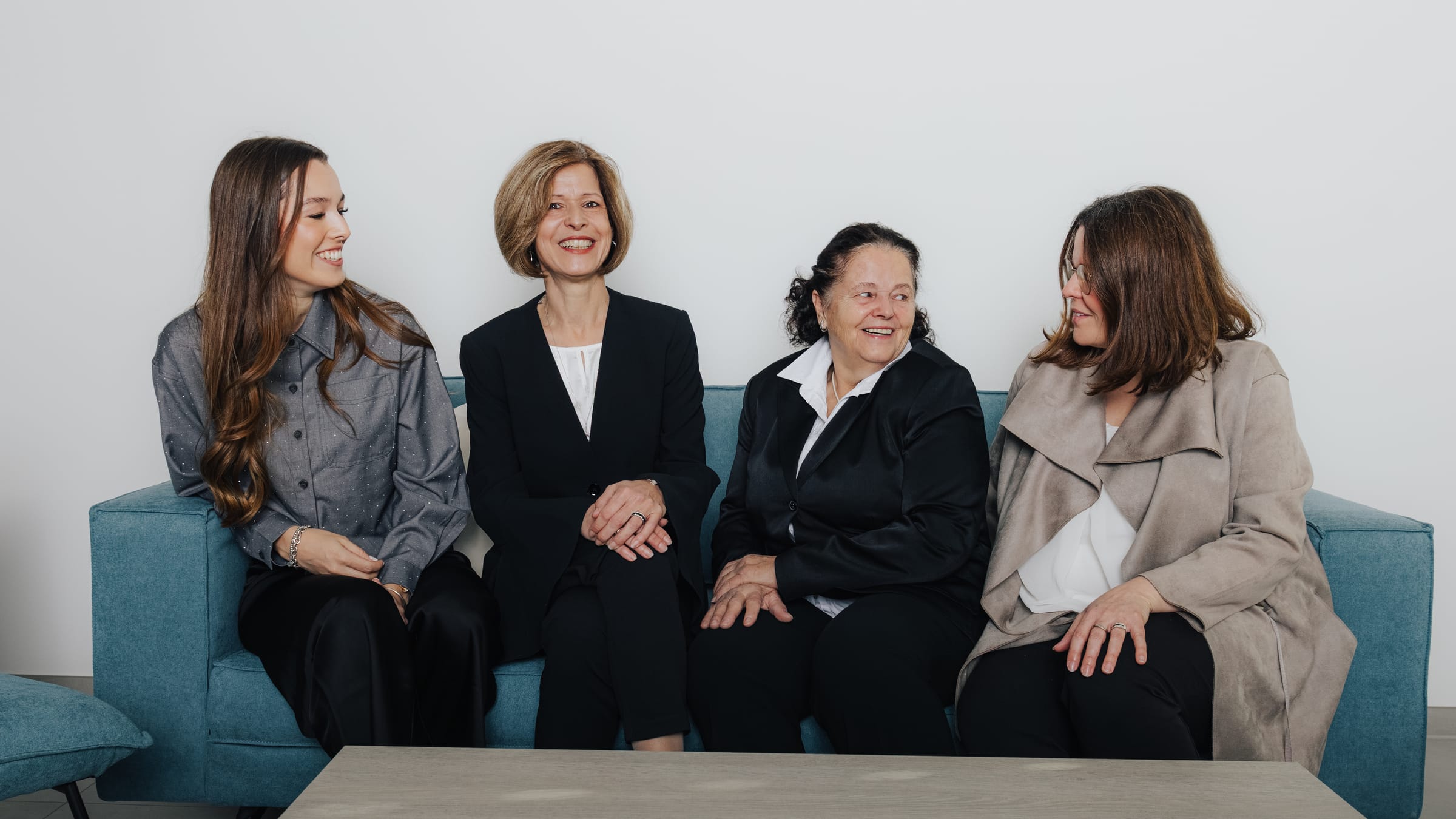 Vier Frauen in formeller Kleidung sitzen auf einem blauen Sofa.