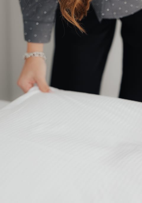 Eine Person glättet die Bettwäsche auf einem Bett.