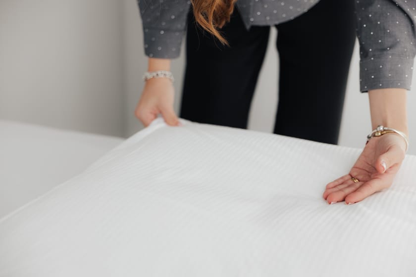 Eine Person glättet die Bettwäsche auf einem Bett.