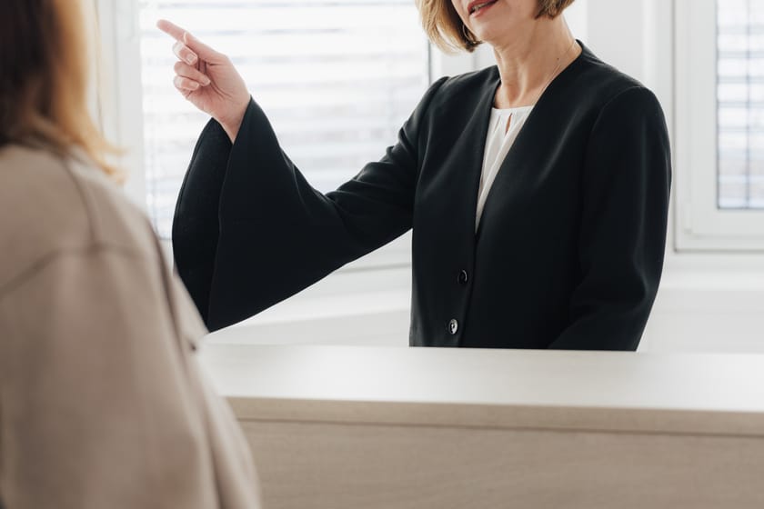 Frau am Empfang weist auf etwas und spricht mit einer anderen Person.