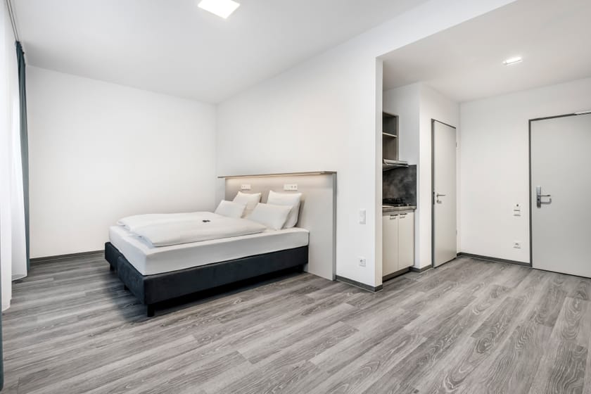 Helles Hotelzimmer mit Doppelbett und Kochnische.