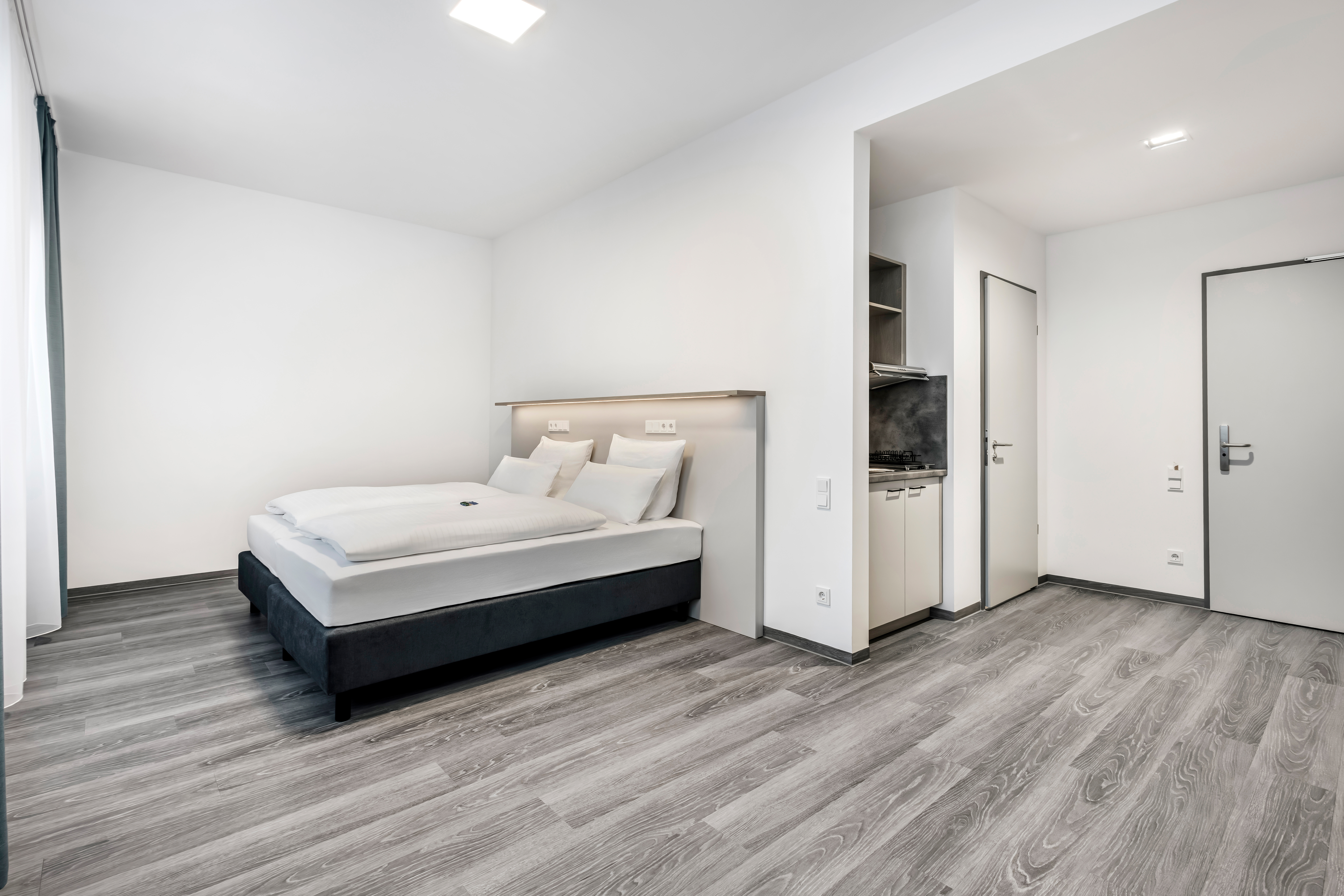 Helles Hotelzimmer mit Doppelbett und Kochnische.