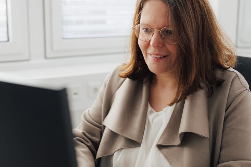 Lächelnde Frau sitzt am Schreibtisch mit Computer.