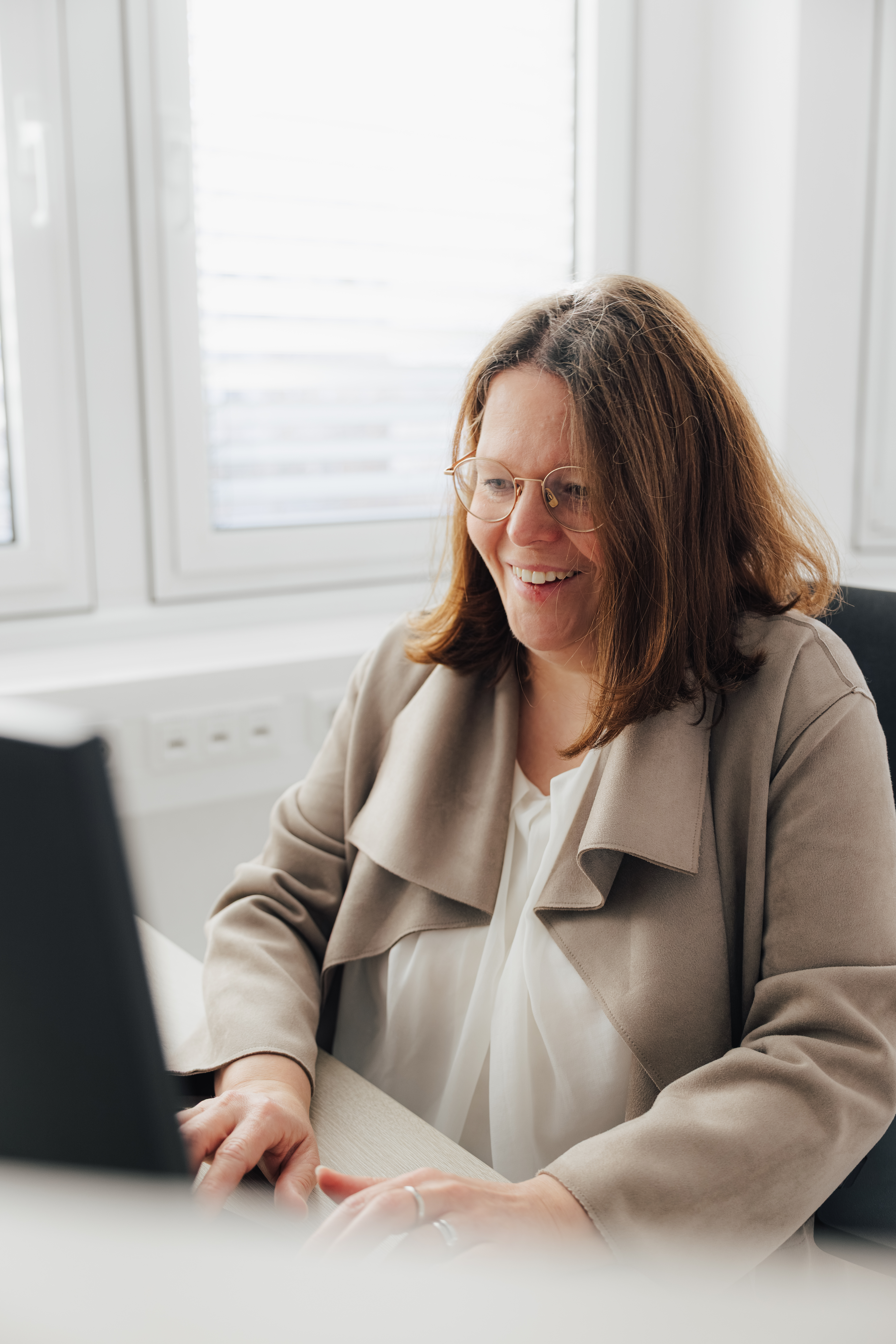 Frau mit Brille sitzt am Schreibtisch und arbeitet am Computer.