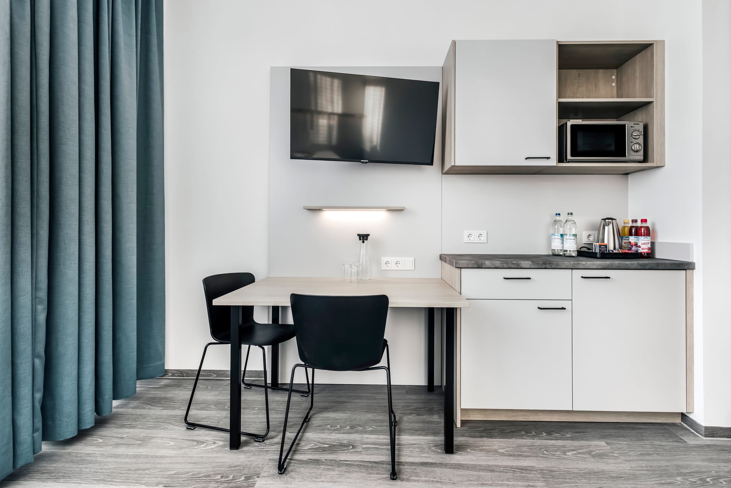 Modernes Hotelzimmer mit Tisch, Stühlen und Küchenzeile.