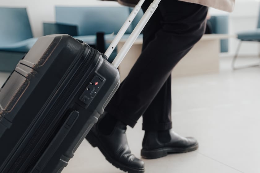 Mann zieht einen schwarzen Koffer in einem hellen Wartebereich.