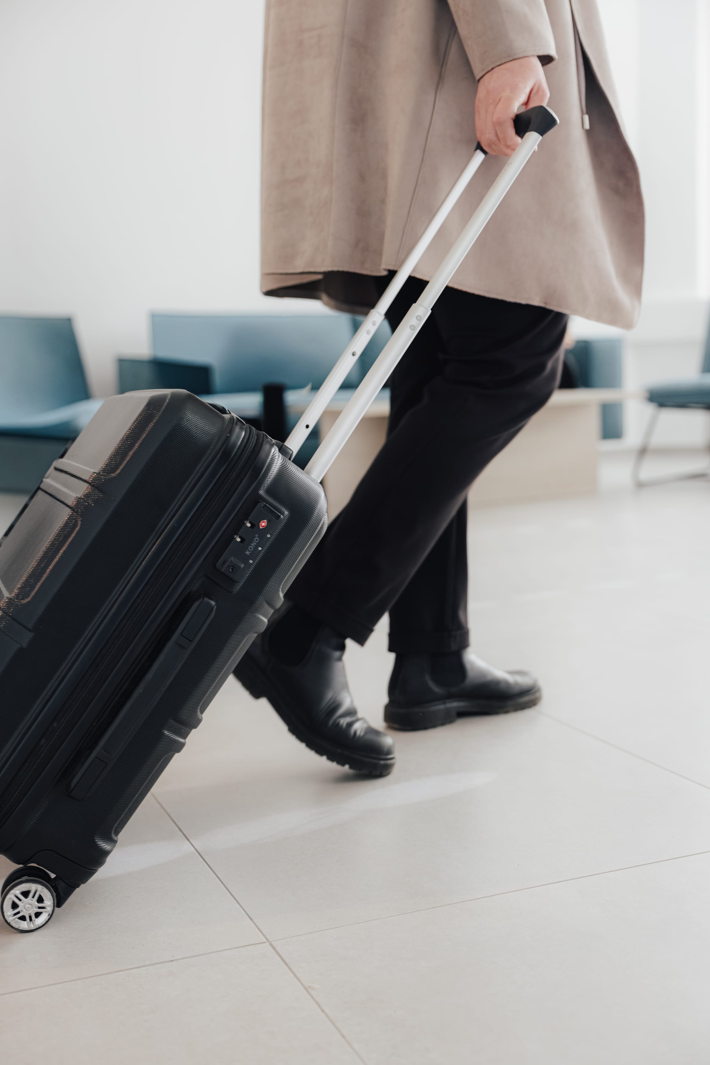 Mann zieht einen schwarzen Koffer in einem hellen Wartebereich.