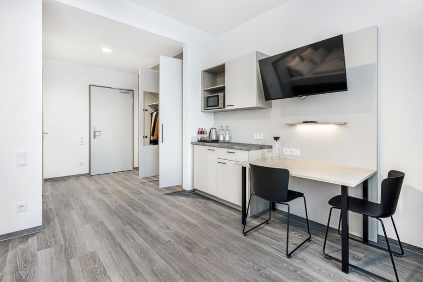 Modernes Hotelzimmer mit Tisch, Stühlen und Fernseher.