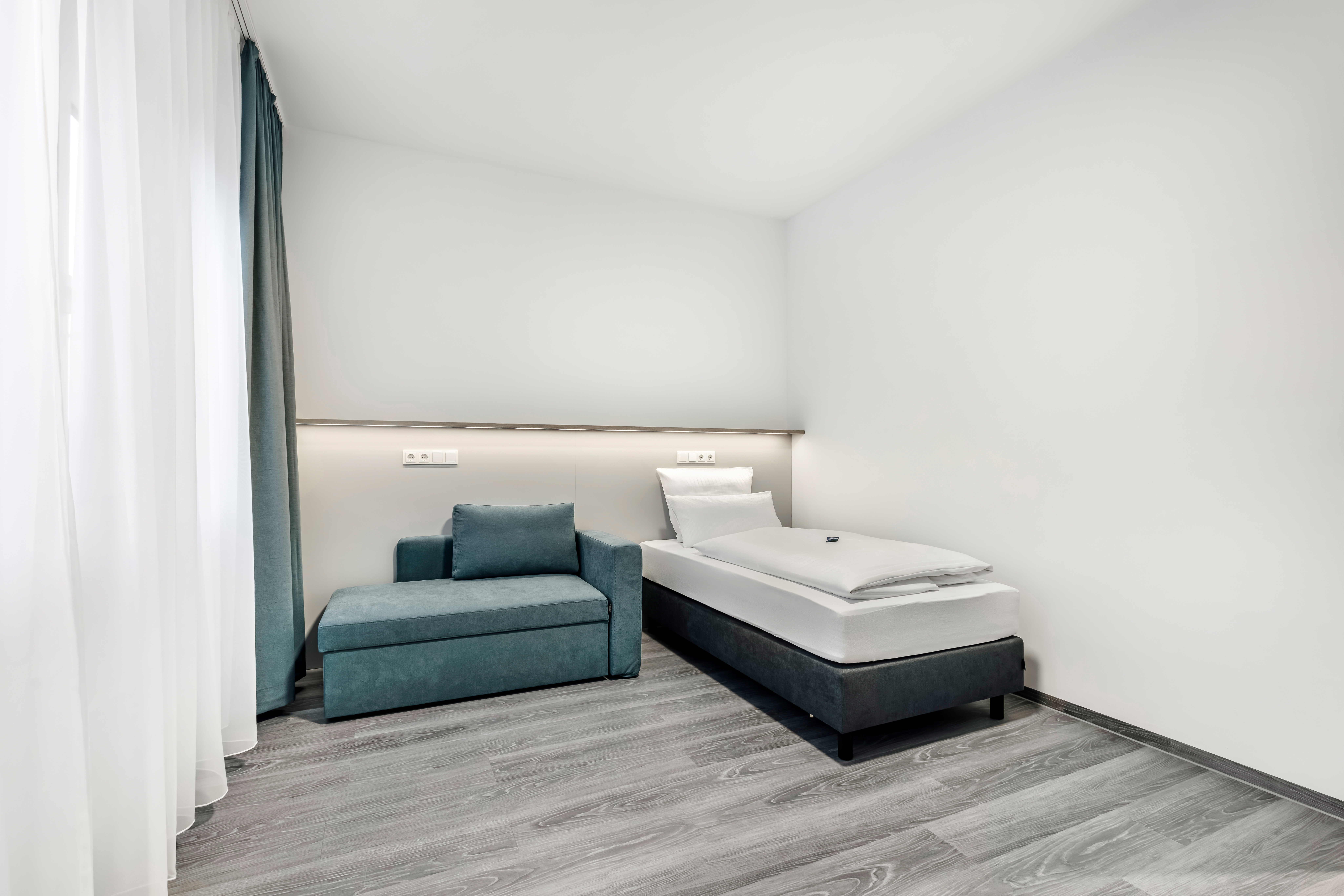 Helles Hotelzimmer mit einem Einzelbett und einem Sessel.