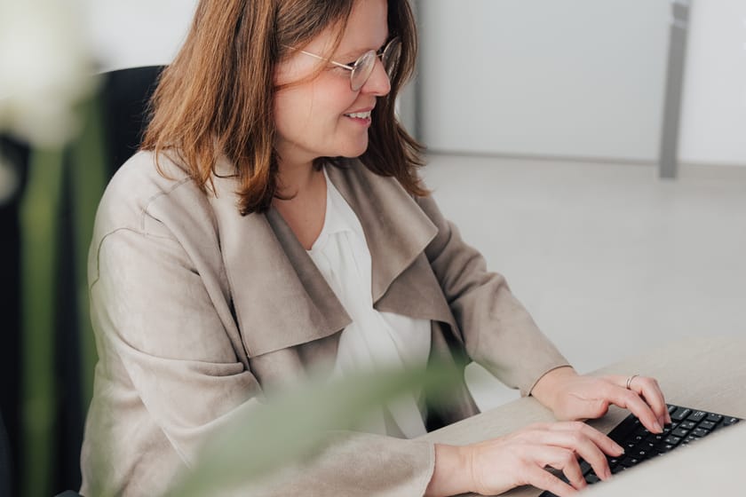 Frau mit Brille tippt an einem Laptop in einem modernen Büro.