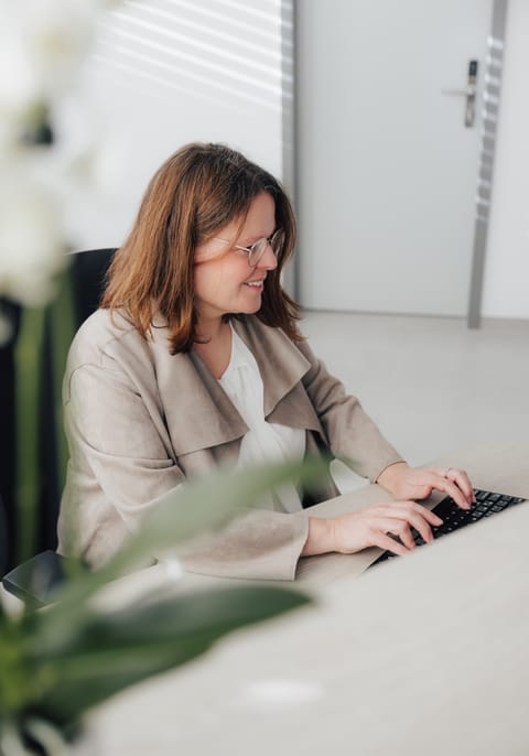 Frau mit Brille tippt an einem Laptop in einem modernen Büro.