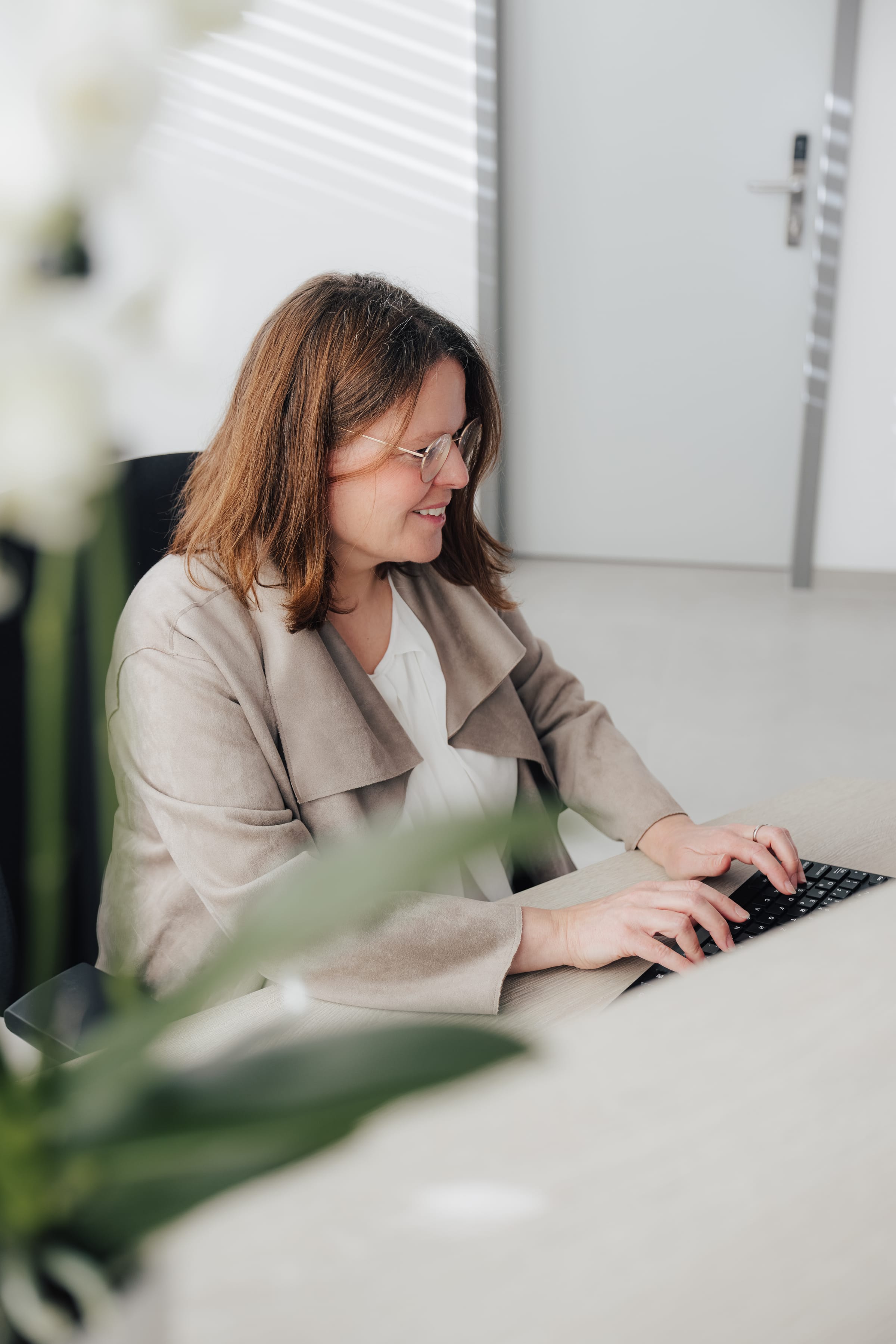 Frau mit Brille tippt an einem Laptop in einem modernen Büro.
