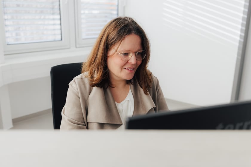 Frau mit Brille sitzt am Schreibtisch und arbeitet am Computer.