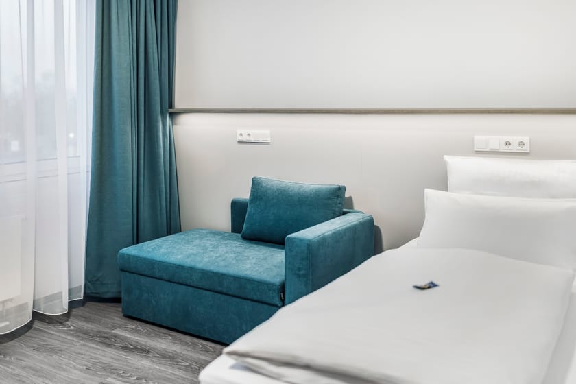 Gemütliches Hotelzimmer mit einem blauen Sessel und einem Bett.
