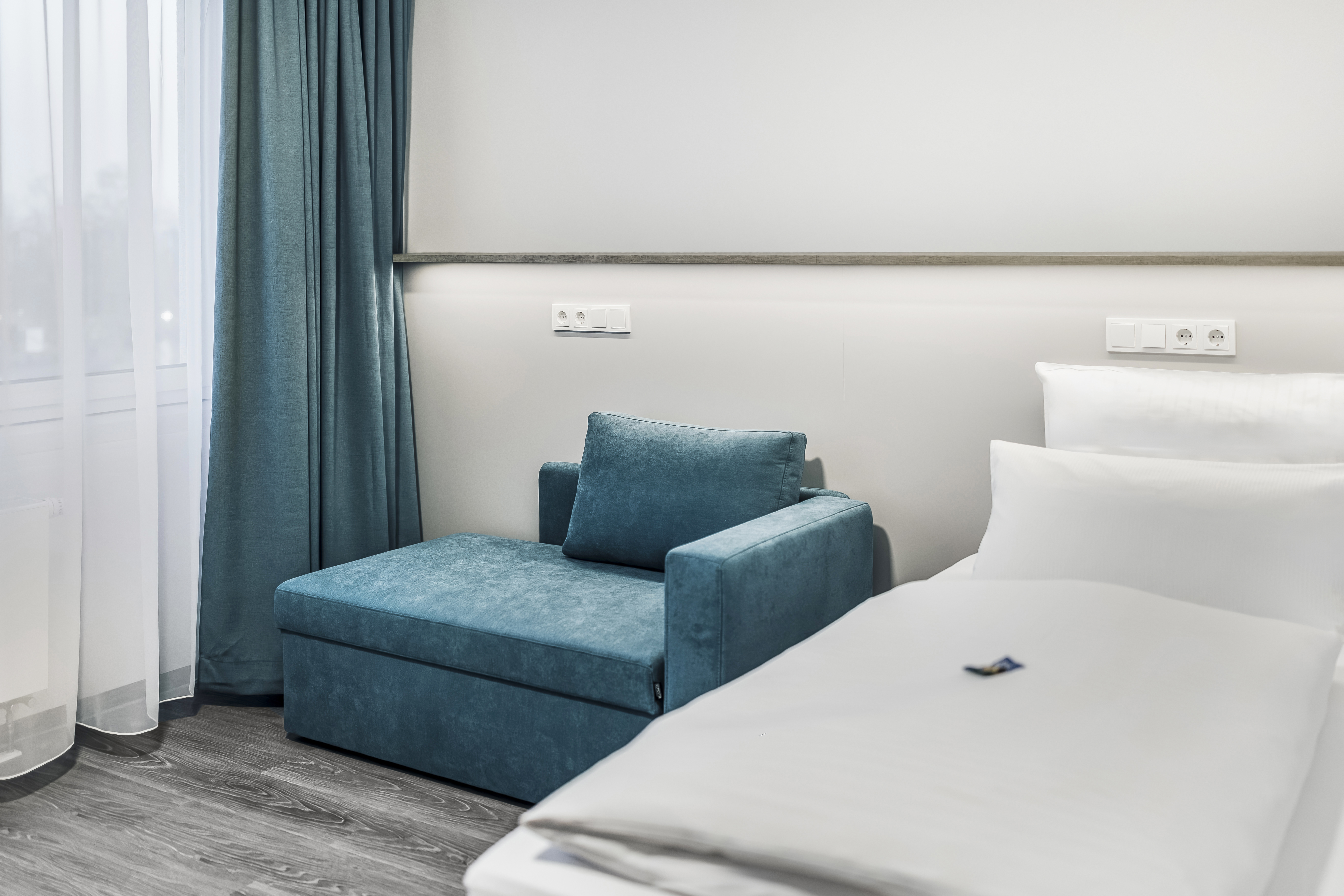 Gemütliches Hotelzimmer mit einem blauen Sessel und einem Bett.