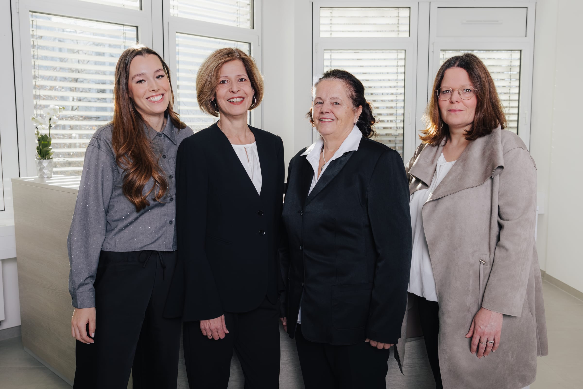 Gruppenbild von vier Frauen in formeller Kleidung vor einem Fenster.