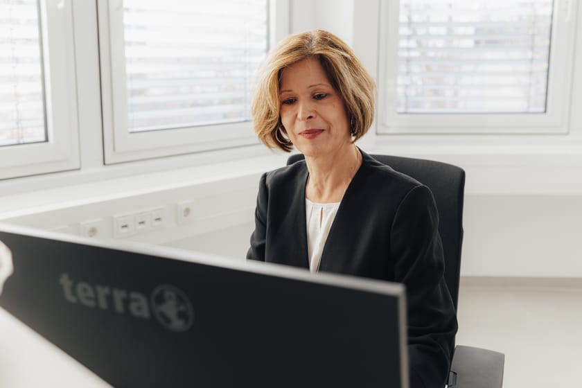 Frau mit blonden Haaren sitzt am Schreibtisch vor einem Computer.