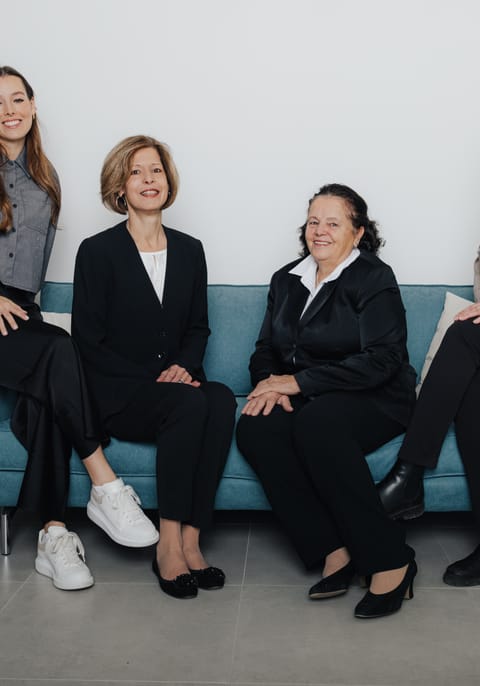 Vier Frauen sitzen auf einem blauen Sofa in einem modernen Raum.