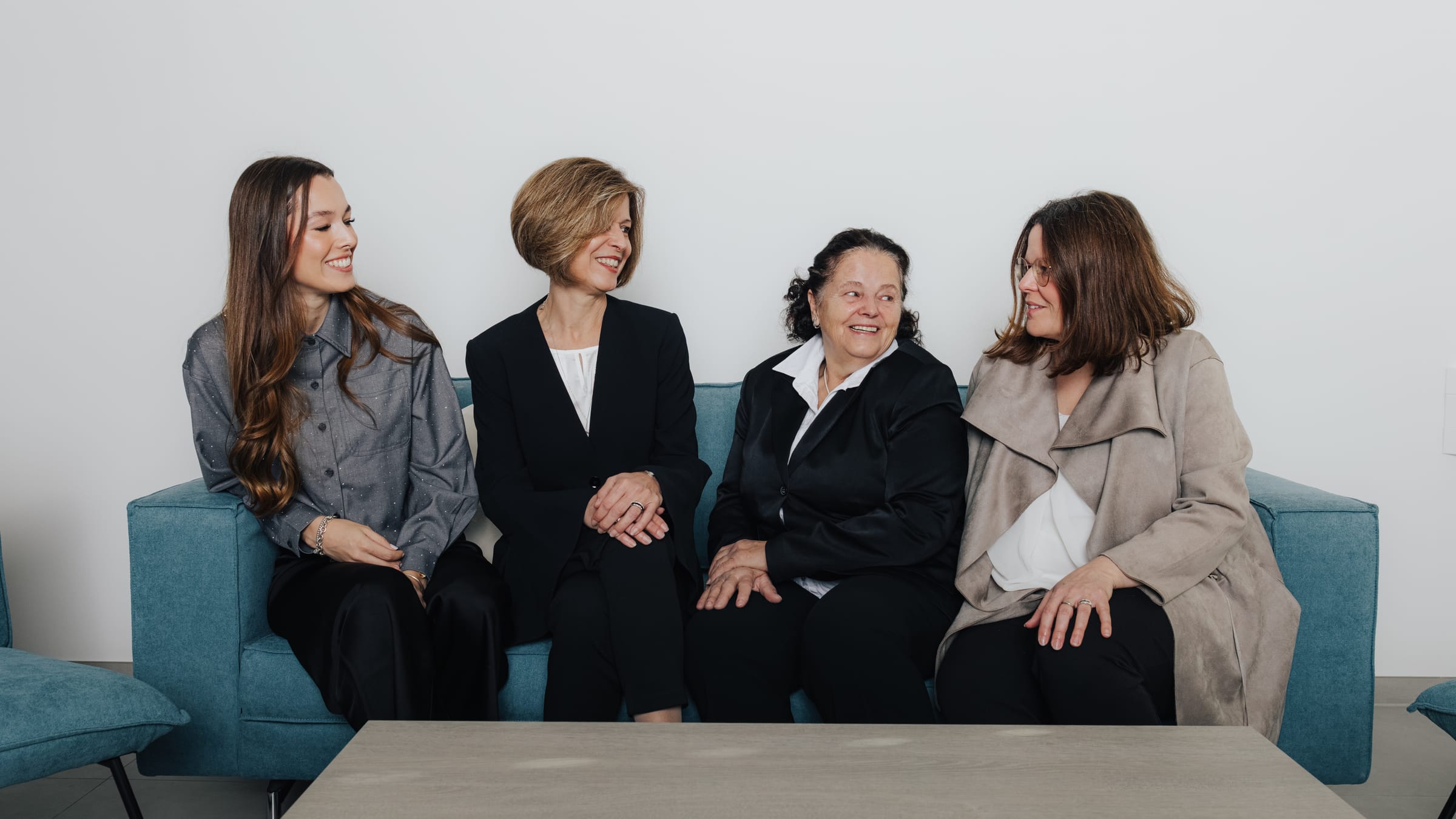 Vier Frauen in formeller Kleidung sitzen auf einem Sofa.