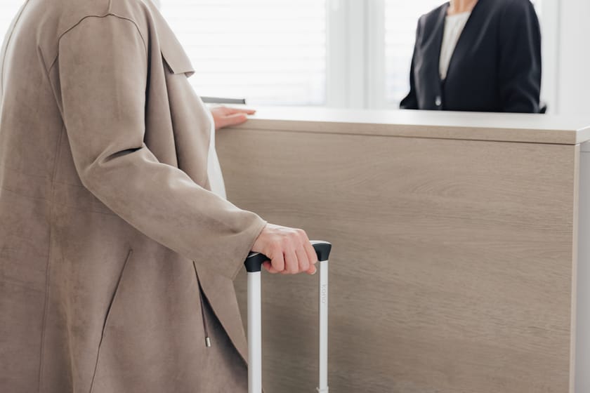 Person am Empfang mit Koffer in der Hand.