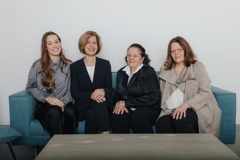 Vier Frauen in Business-Kleidung sitzen auf einem Sofa.