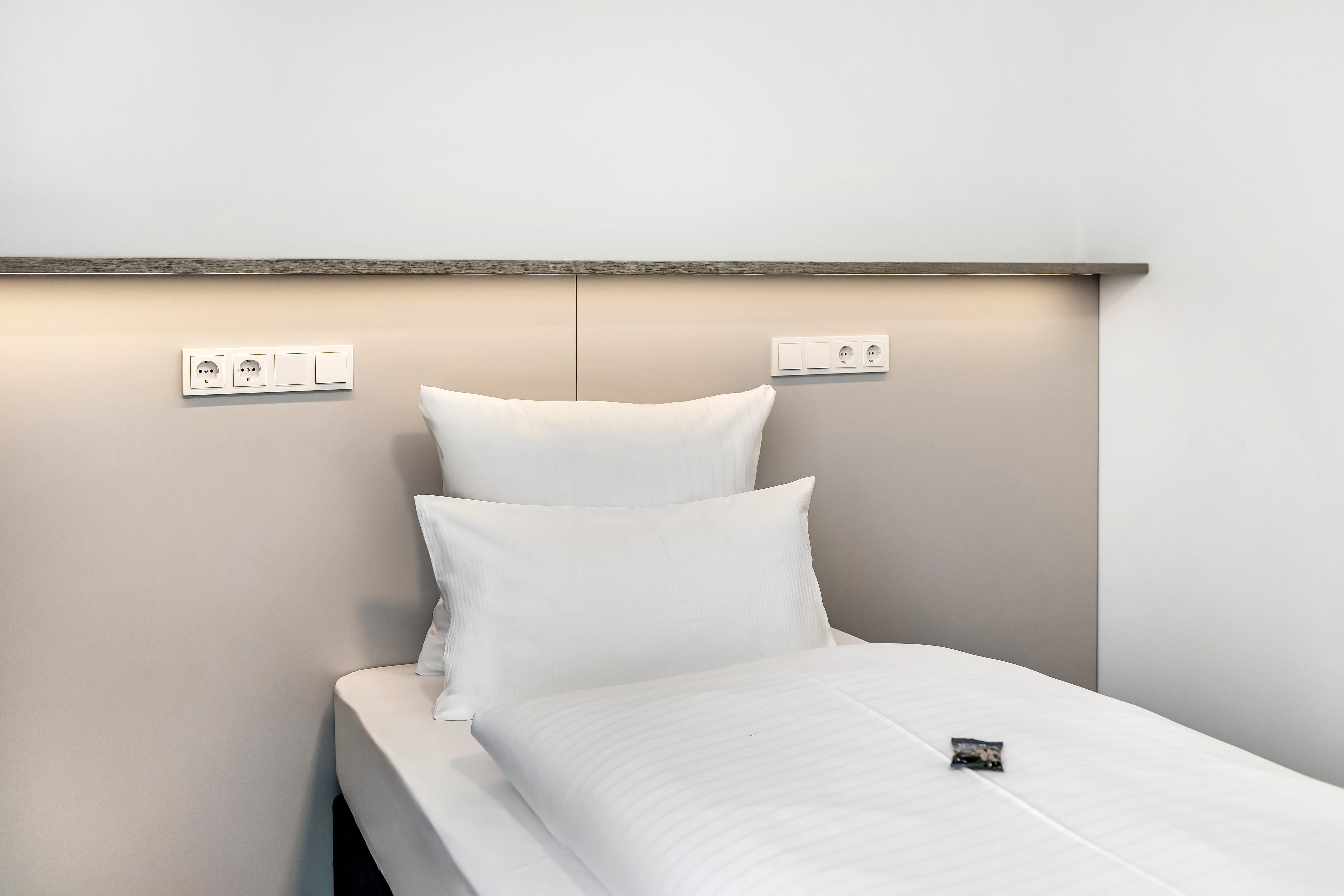 Einzelbett in modernem Hotelzimmer mit Kissen und Beleuchtung.